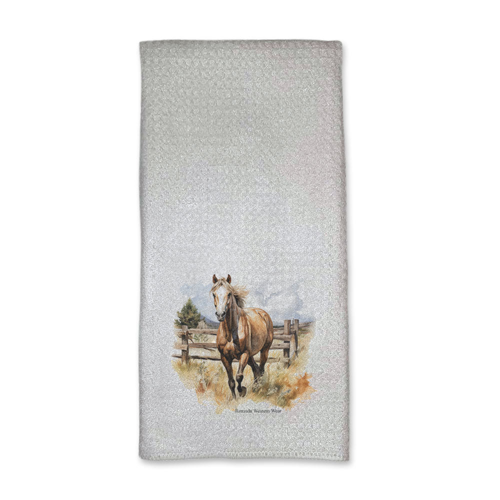 A vibrant western style kitchen hand towel featuring a beautiful palomino horse running in a field with a wooden fence behind him. Comes in a white color. The design captures the spirit of western culture.